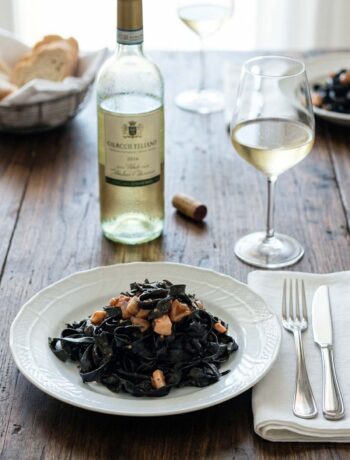 piatto di tagliatelle al nero di seppia con bottiglia. e calice di vino bianco