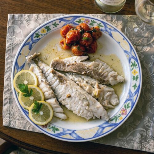 piatto con orata al cartoccio, limone con bottiglia di vino e pomodorini