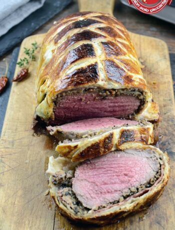 Filetto alla Wellington tagliato a fette spesse, con la carne rosa, lo strato di funghi e la crosta di sfoglia dorata
