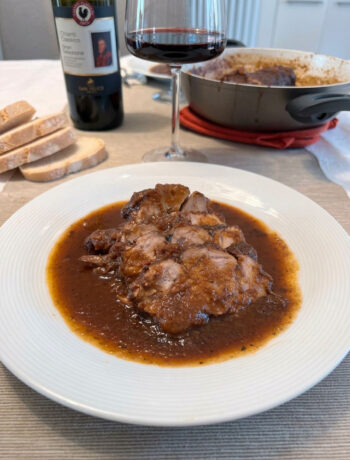 Fette di stracotto al Chianti con la salsa scura di vino e verdure, accanto a un bicchiere di Chianti e pane toscano