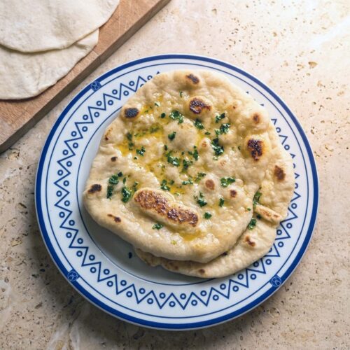 Pane naan fatto in casa con bolle dorate e macchie scure, spennellato di burro e aglio, con foglie di coriandolo